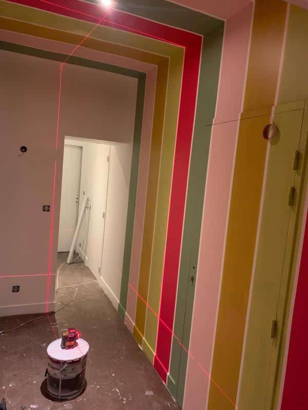 Mur intérieur présentant un design créatif de bandes de peinture multicolores formant un motif de cadre dans une perspective de couloir en construction.